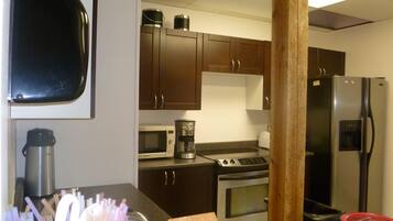 A kitchen with dark wooden cabinets, a stainless steel refrigerator, a microwave, a coffee maker, and a toaster.