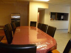 A conference room with a long table, black chairs, a refrigerator, and a window with blinds. - Vernon Hostel (Vernon)