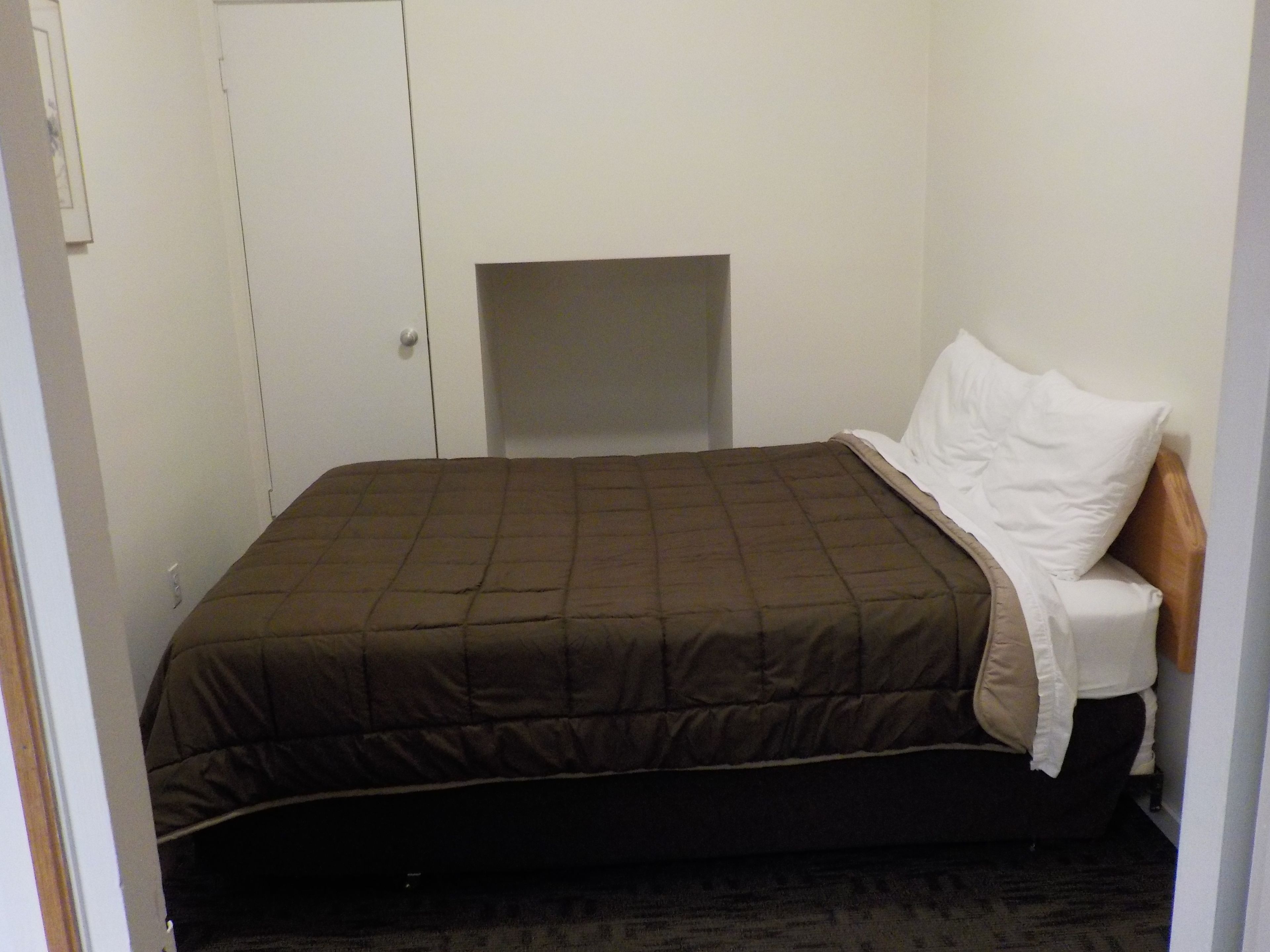 A single bed with a brown quilt, a white pillow, and a wooden headboard.