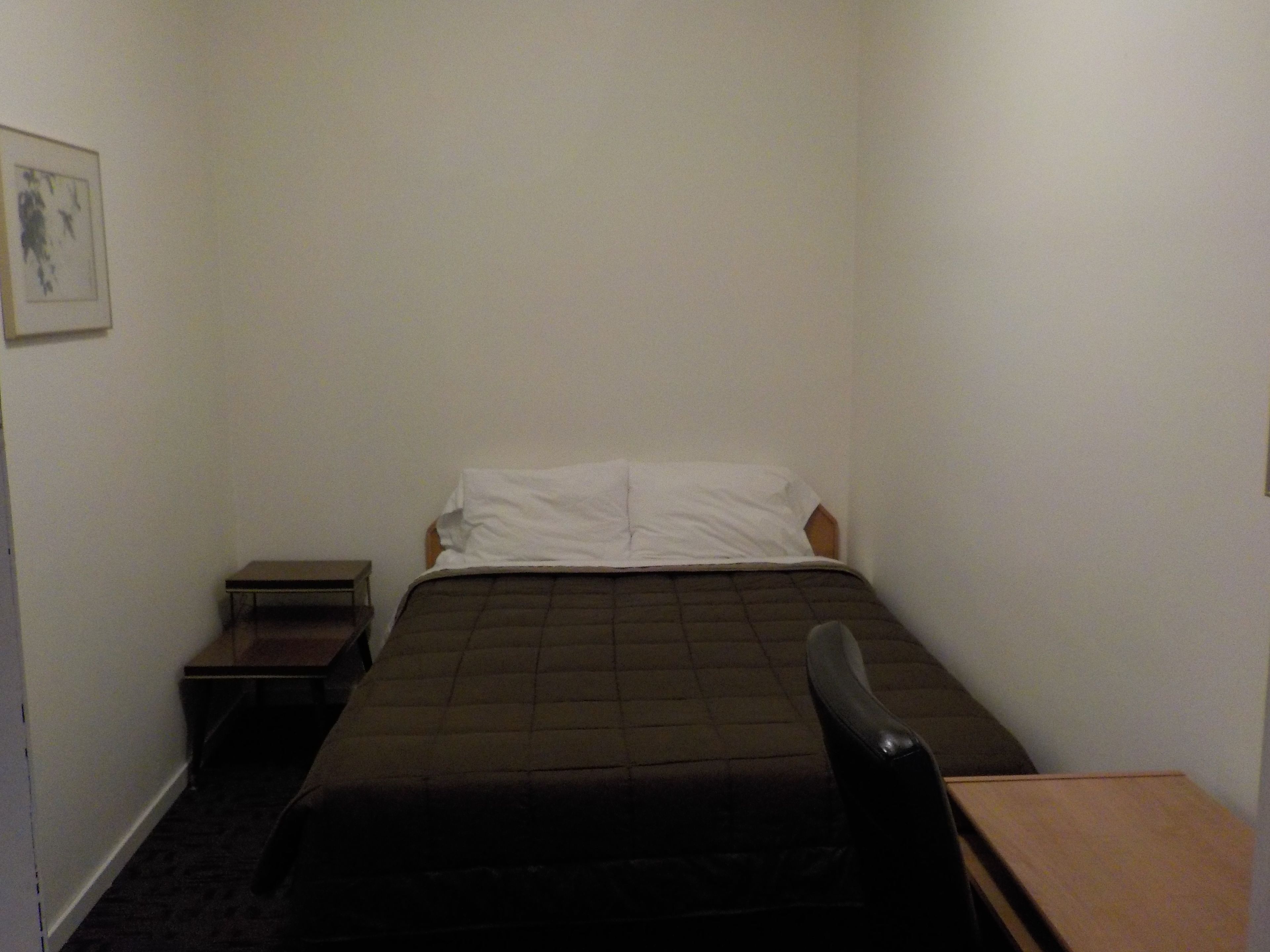 A small, single-bed room with a wooden headboard, a bedside table, and a chair.