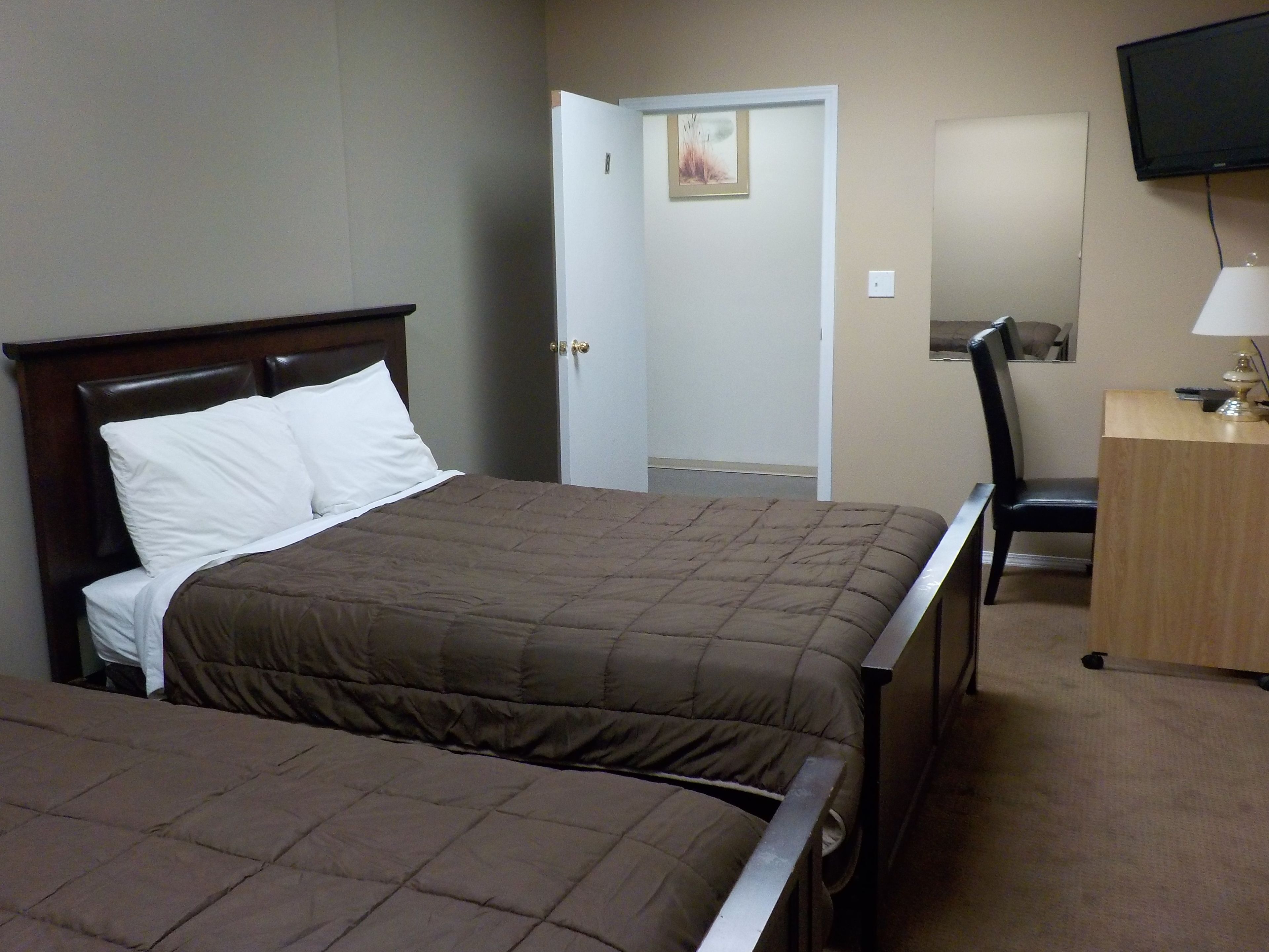 A hotel room with two beds, a desk, a chair, and a television.