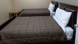 A hotel room with two beds, a small wooden table, and a wall-mounted coat rack. - Vernon Hostel (Vernon)