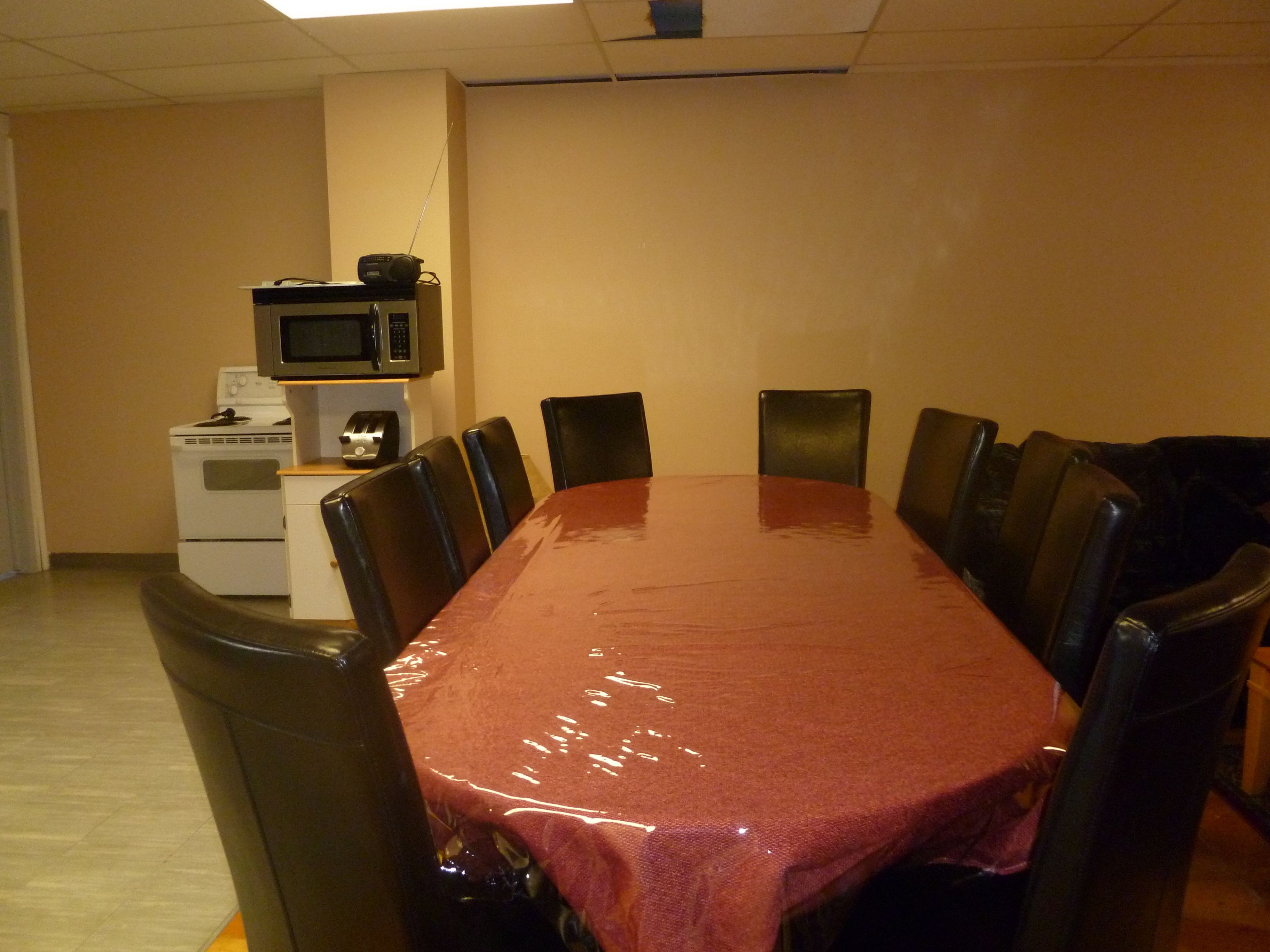 A conference room with a long table, chairs, a microwave, and a small kitchenette.
