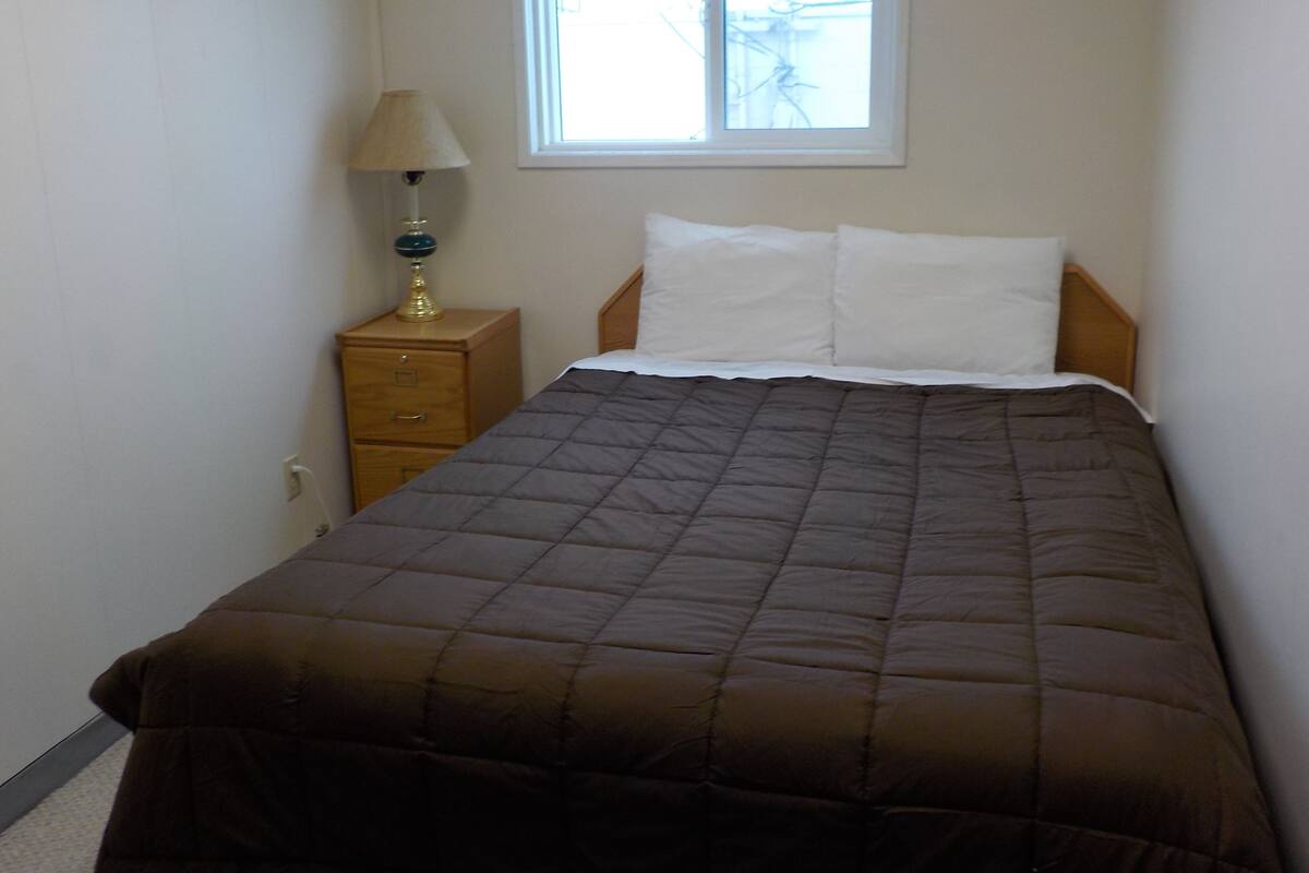 Un dormitorio con una cama, una mesita de noche, una lámpara y una ventana.