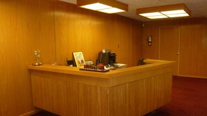 A reception desk with a wooden finish, a clock, and a framed picture on the counter. - Vernon Hostel (Vernon)