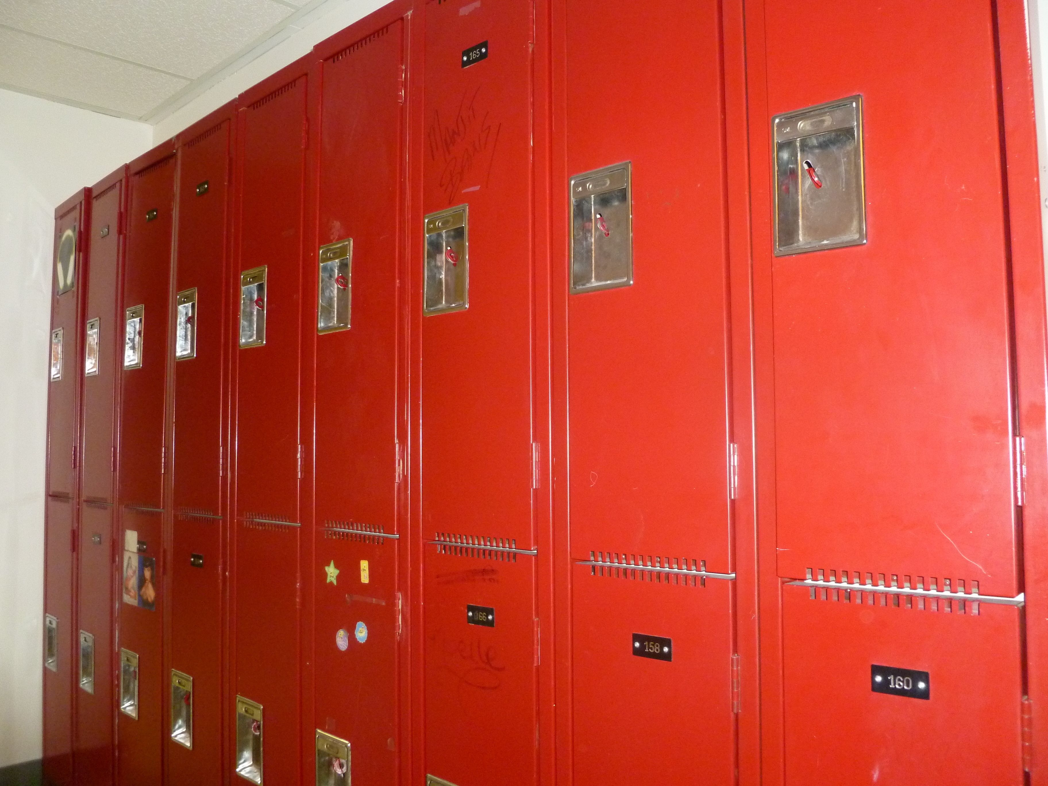 A row of red lockers with numbered labels, each with a small window and a lock.
