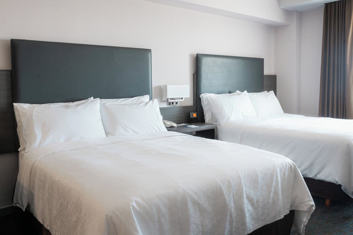Une chambre d’hôtel avec deux lits simples, une table de chevet avec une lampe et une fenêtre avec des rideaux.