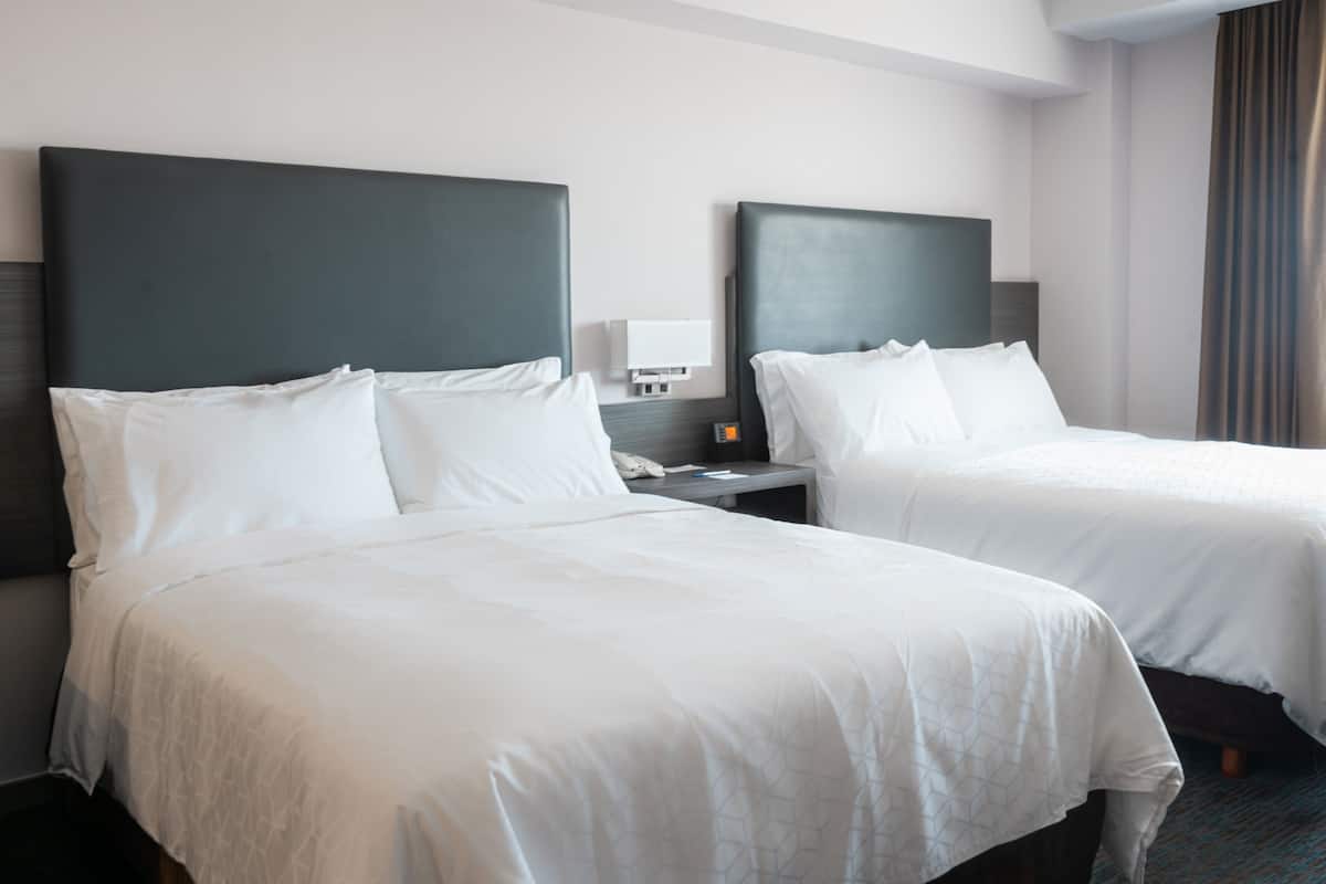 A hotel room with two single beds, a nightstand with a lamp, and a window with curtains.