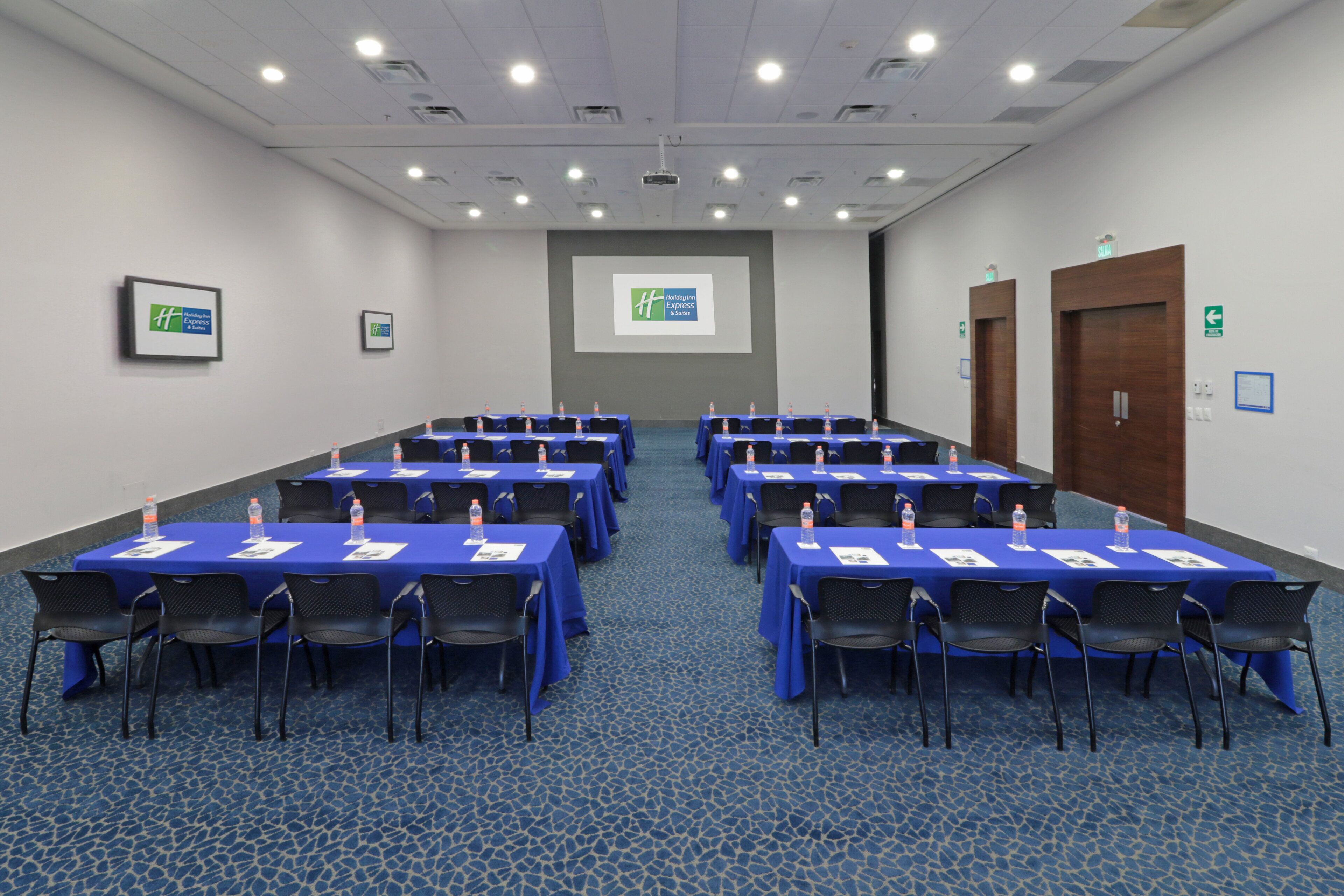 A conference room with multiple tables and chairs, a projector screen, and a carpeted floor.