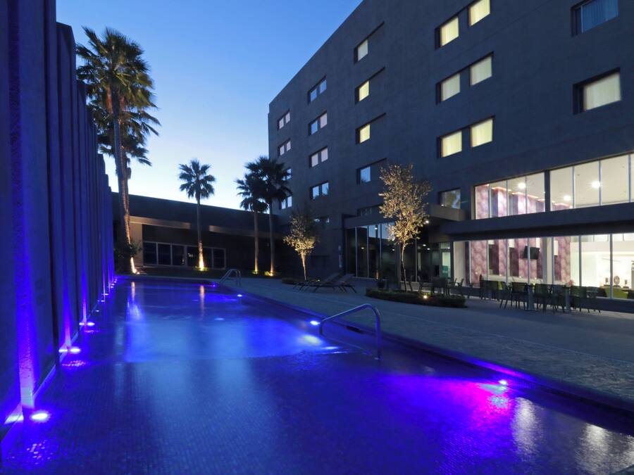 Una piscina de diseño moderno, rodeada por un edificio con múltiples ventanas y algunas palmeras.