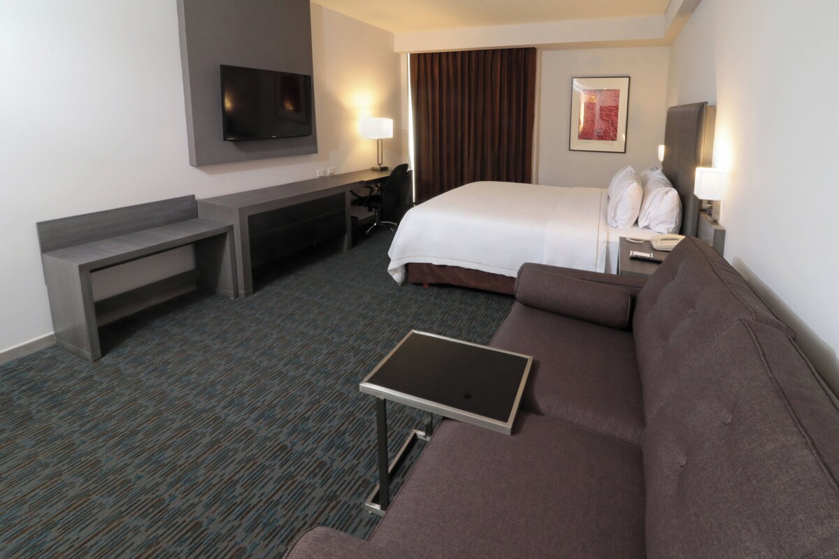 A hotel room with a bed, a desk, a TV, a sofa, and a small table.