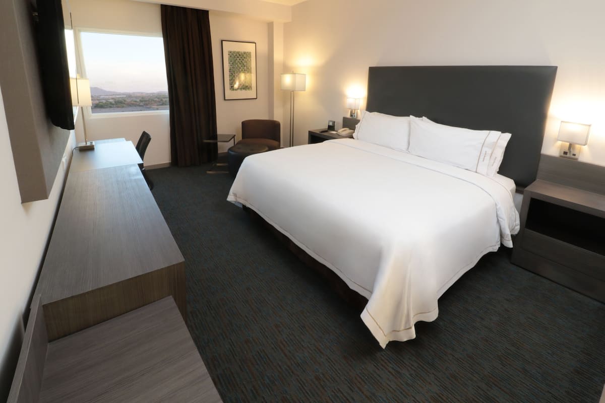 A hotel room with a large bed, a desk, a chair, and a view of the outdoors.