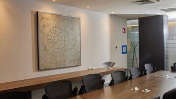 A conference room with a long table, chairs, a large abstract painting, and a door with a glass panel.
