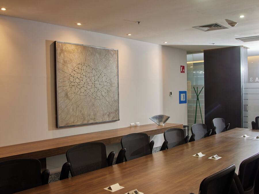 A conference room with a long table, chairs, a large abstract painting, and a door with a glass panel.