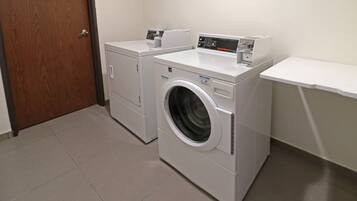 Un cuarto de lavandería con dos lavadoras y una secadora, una puerta de madera y un estante blanco.