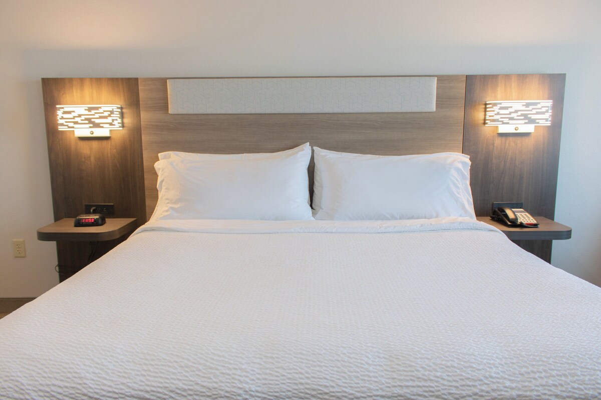 A neatly made bed with white linens, two bedside tables with lamps, and a wall-mounted light fixture above the bed.