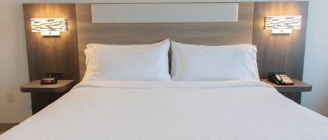 Una cama bien hecha con sábanas blancas, dos mesitas de noche con lámparas, y un aplique en la pared sobre la cama.