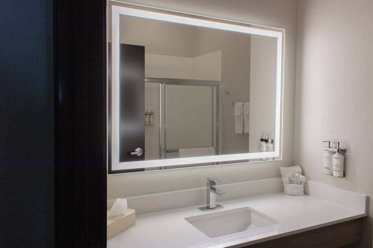 A modern bathroom with a large mirror, a sink, and a shower area.