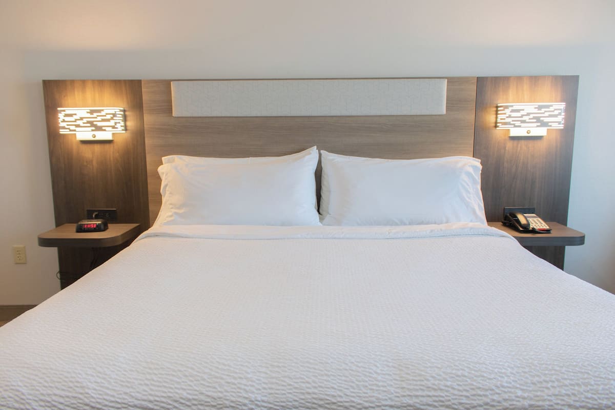 A neatly made bed with white linens, two bedside tables with lamps, and a wall-mounted light fixture above the bed.