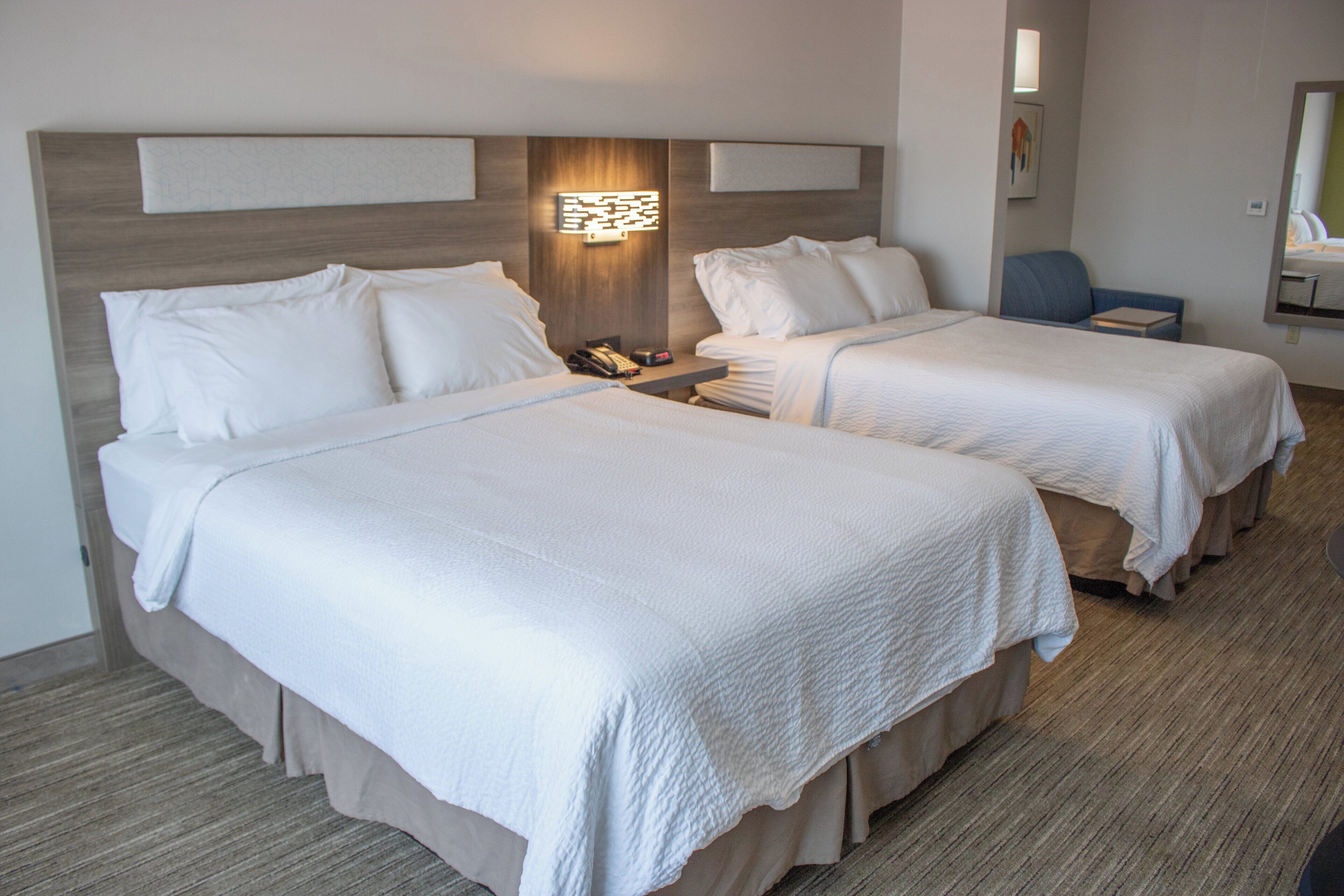 A hotel room with two beds, a nightstand, a chair, and a mirror.