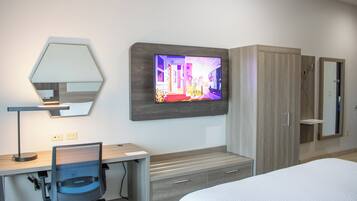 A hotel room with a bed, a desk with a chair, a television mounted on the wall, a wardrobe, and a mirror.