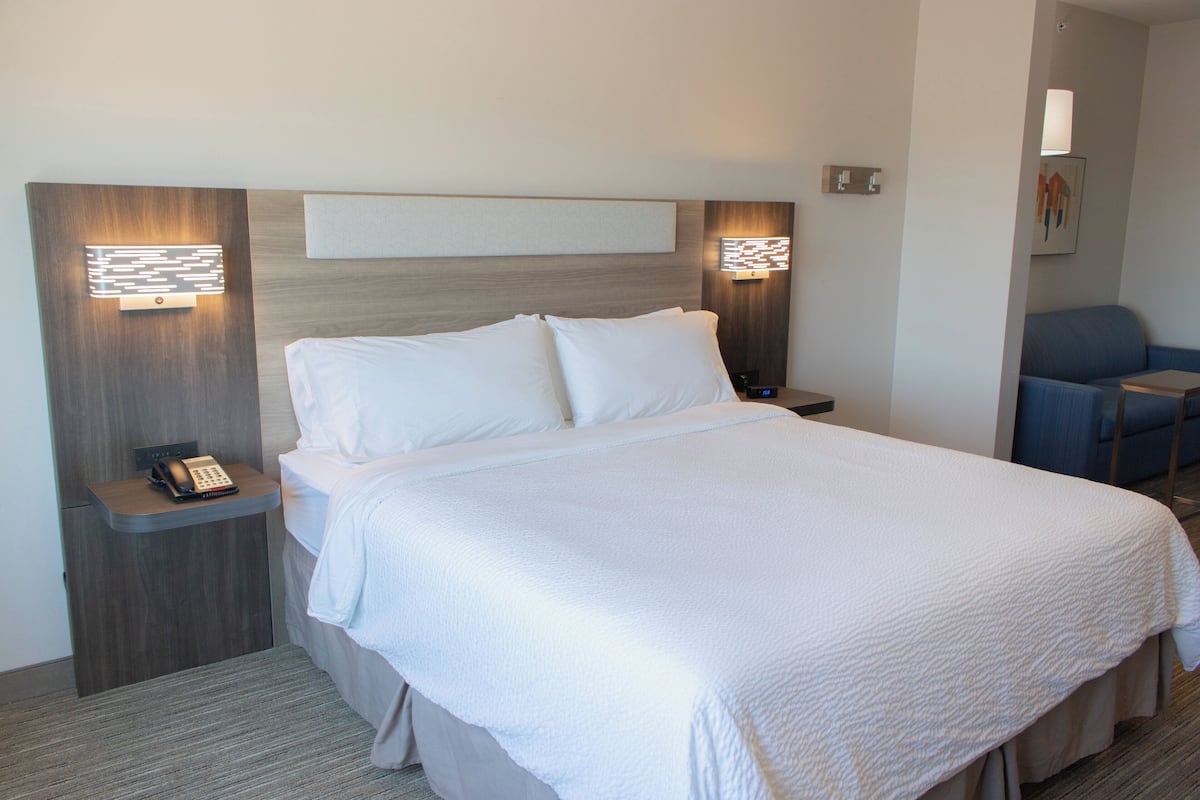A hotel room with a large bed, two bedside tables with lamps, a chair, and a wall-mounted artwork.