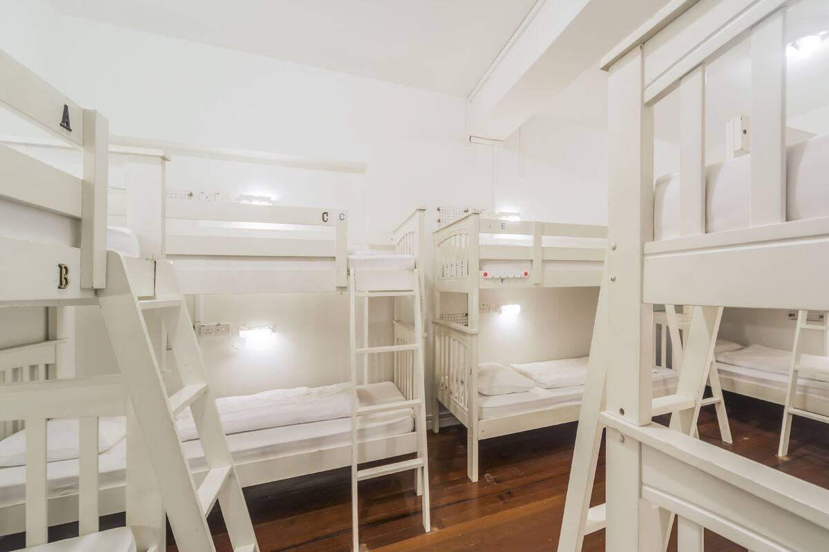A room with bunk beds, wooden flooring, and white walls.