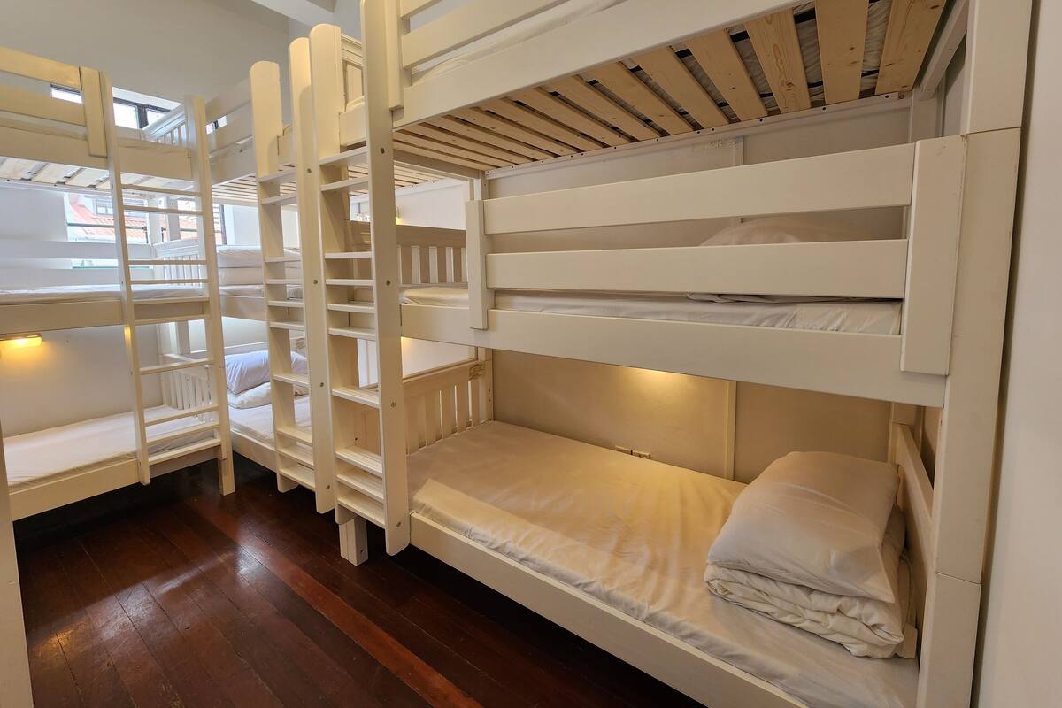 A bunk bed room with a wooden ladder, white bedding, and a view of the outside through a window.