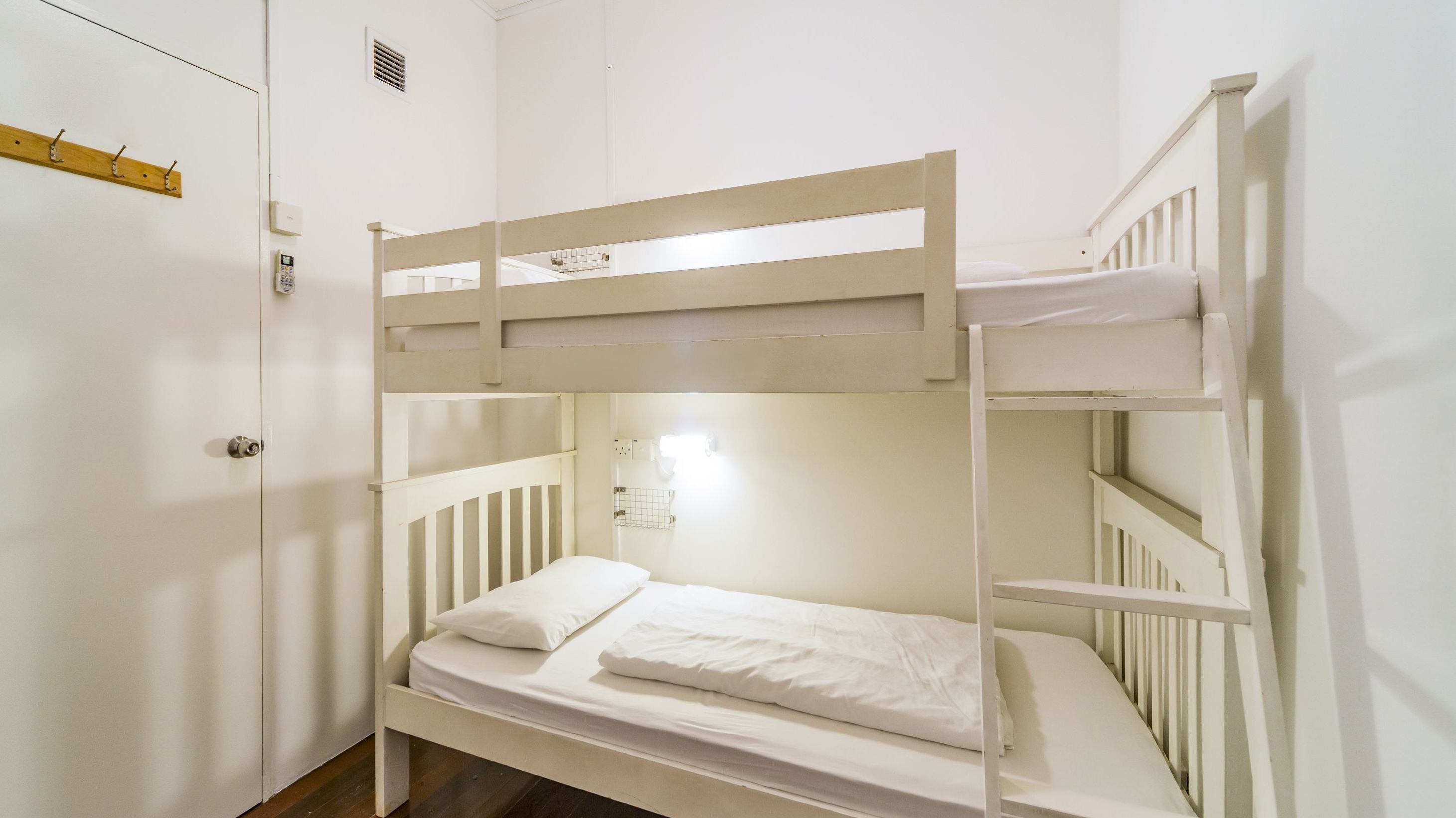 Una cama litera con ropa de cama blanca en una habitación con paredes blancas y una puerta de madera.