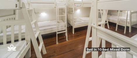 Dormitorio compartido para 10 personas con literas y camas individuales, suelo de madera y paredes blancas.