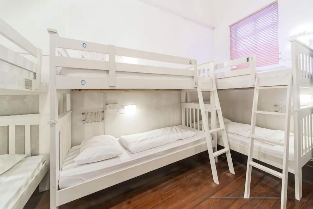A bunk bed room with a ladder, wooden floor, and a window with blinds.