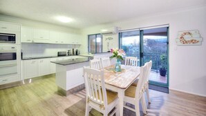 Una cocina moderna con armarios blancos, una isla central y un comedor con sillas blancas.