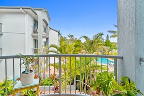 A balcony with a view of a pool and tropical plants. - Pacific Place Apartments (Bilinga)