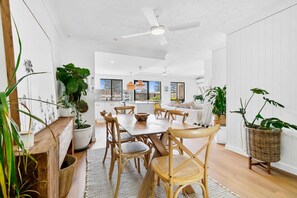 A modern kitchen with white cabinets, a dining table with chairs, and a ceiling fan. - Pacific Place Apartments (Bilinga)
