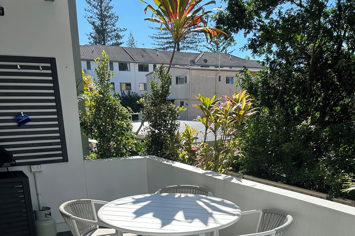 Un patio exterior con una mesa redonda y cuatro sillas, rodeado por un muro blanco y un piso negro.