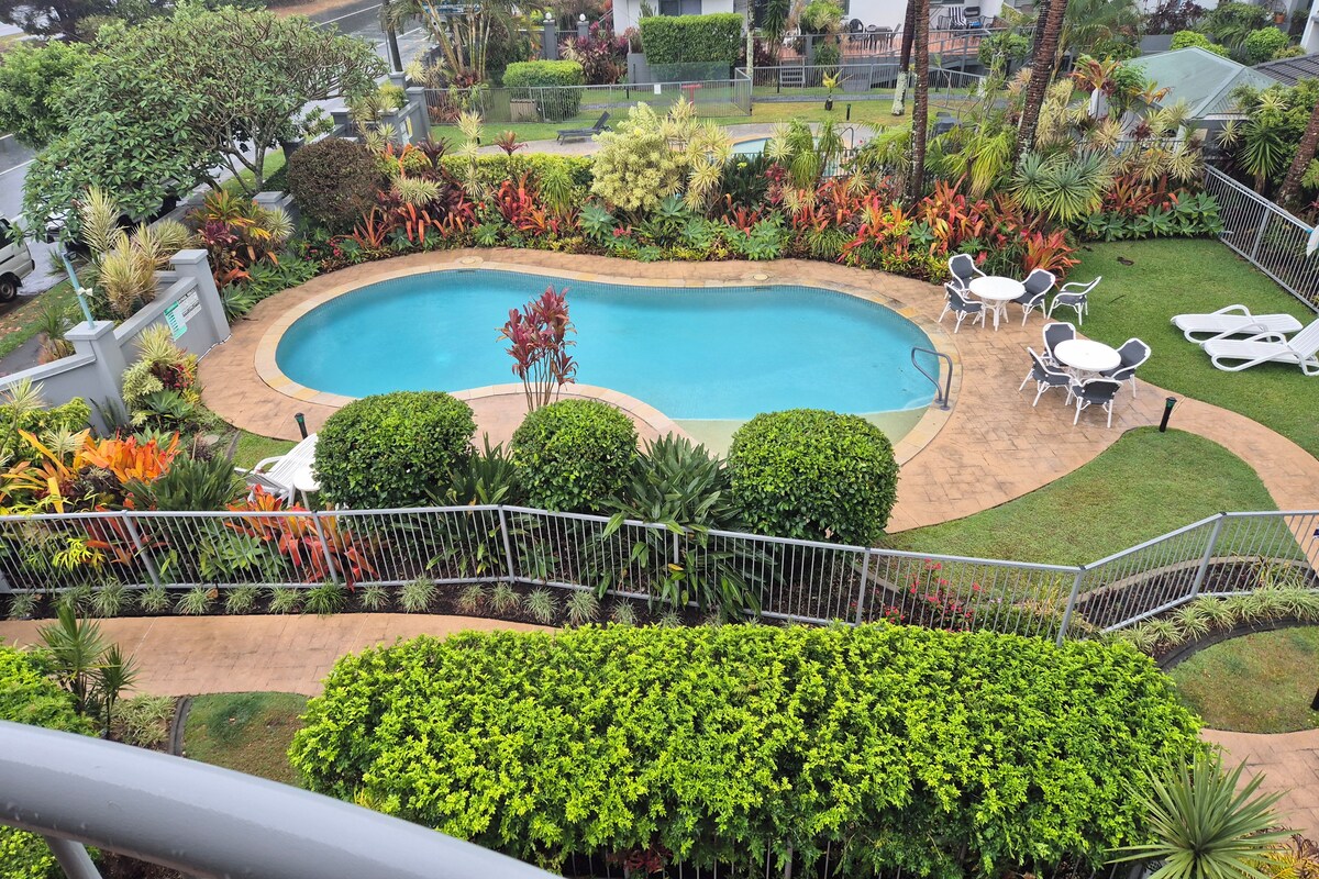 Una piscina rodeada de exuberante vegetación, con una zona de terraza y sillones de descanso.
