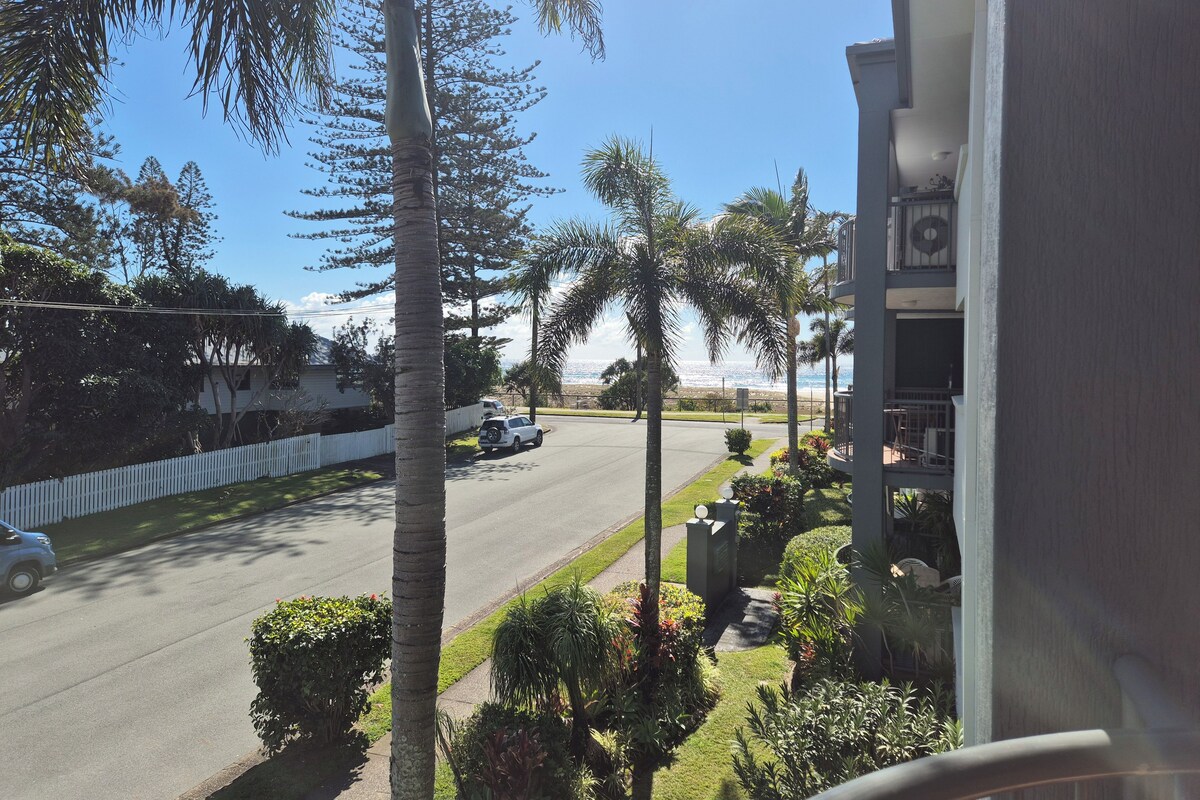 Un barrio residencial con una calle, palmeras y vista al océano.
