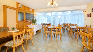 A dining area with wooden tables and chairs, a chandelier, and large windows. - Pension Villa Stella (Spindleruv Mlyn)