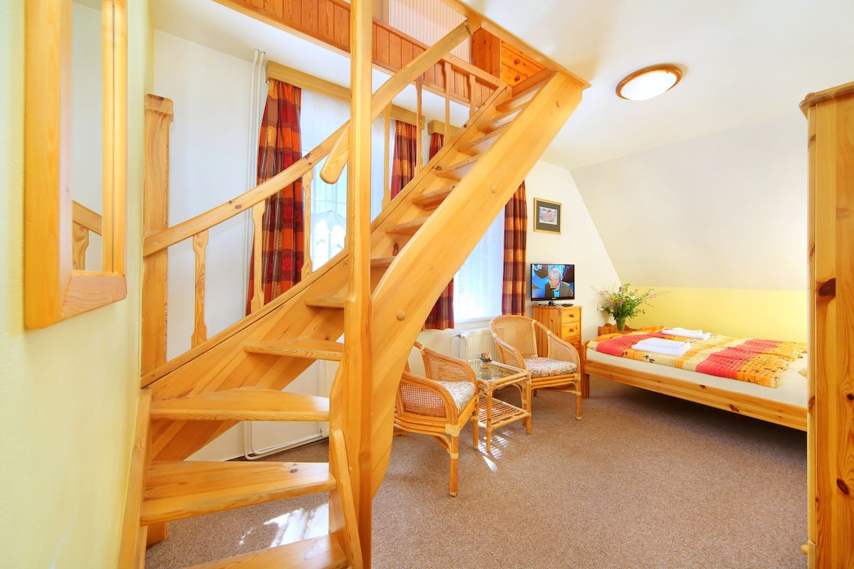 A wooden staircase leading to a loft bedroom with a bed, two chairs, and a small table.