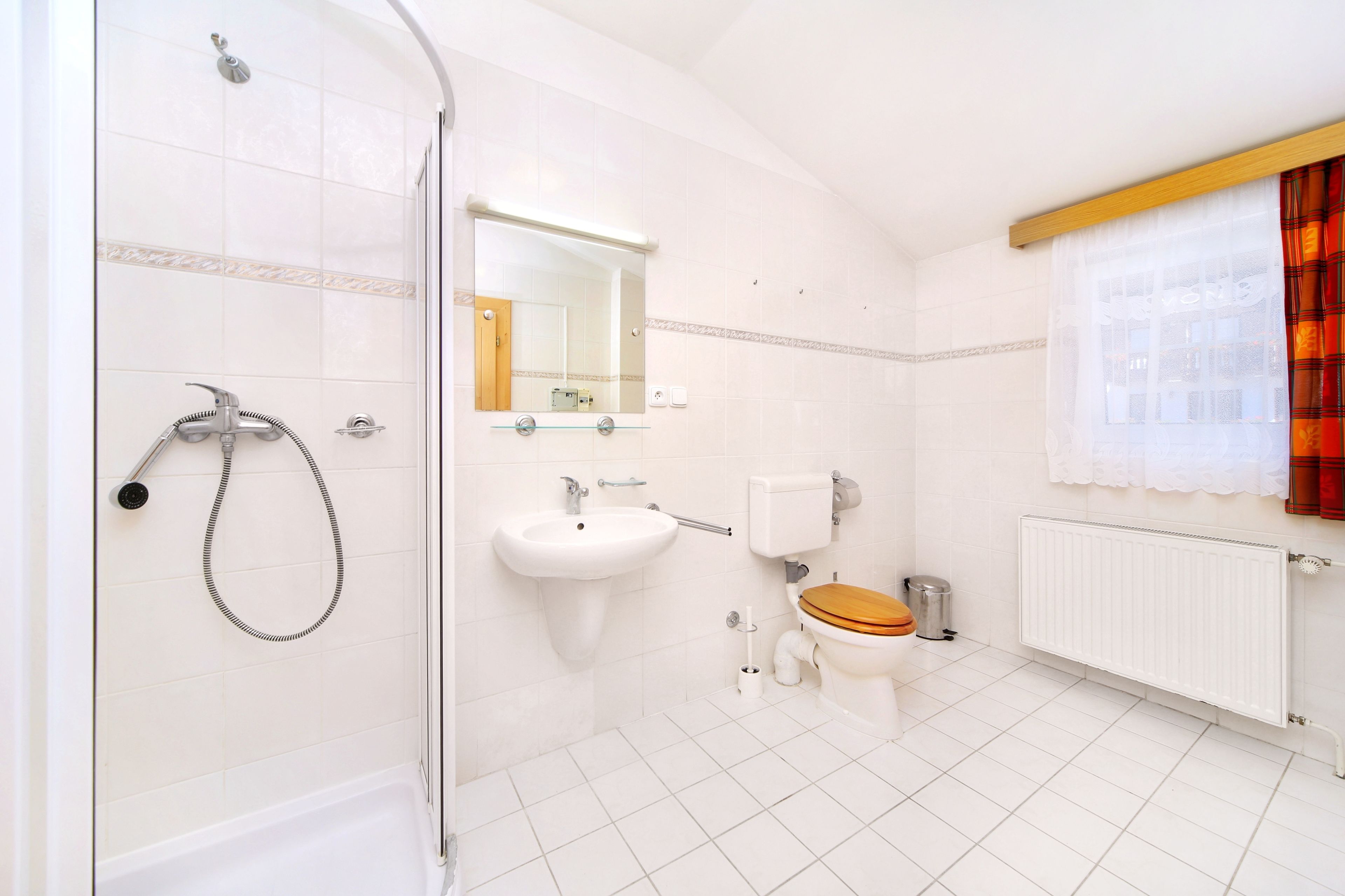 A bathroom with a shower, sink, toilet, and a window with curtains.