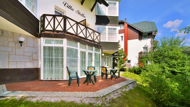 A two-story building with a balcony and a patio area with outdoor seating. - Pension Villa Stella (Spindleruv Mlyn)