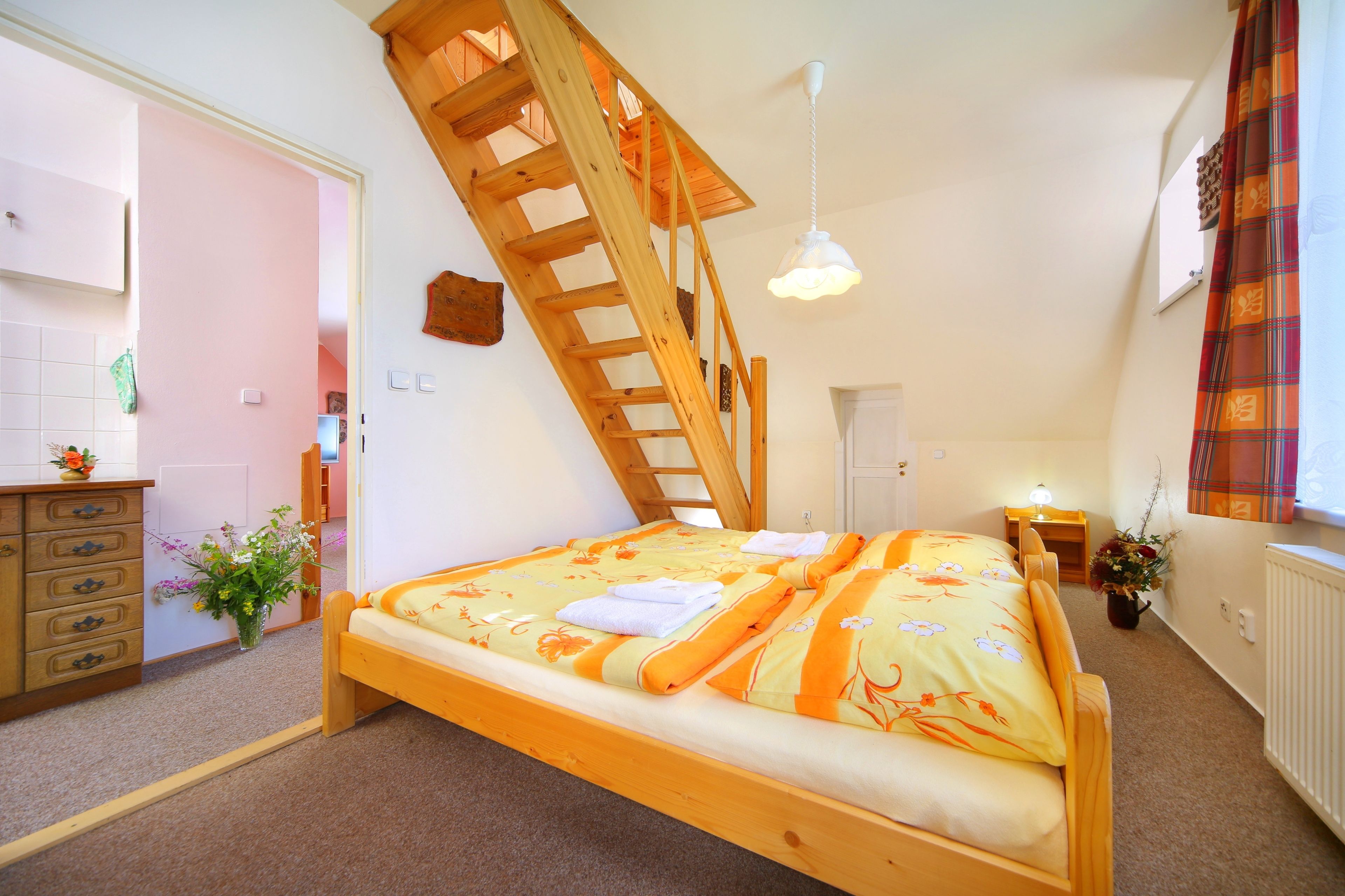 Un dormitorio con una cama de madera, una escalera de madera, una mesita de noche con lámpara y una ventana con cortinas.