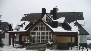 A snow-covered house with a large front window, a chimney, and a garage. - Pension Villa Stella (Spindleruv Mlyn)