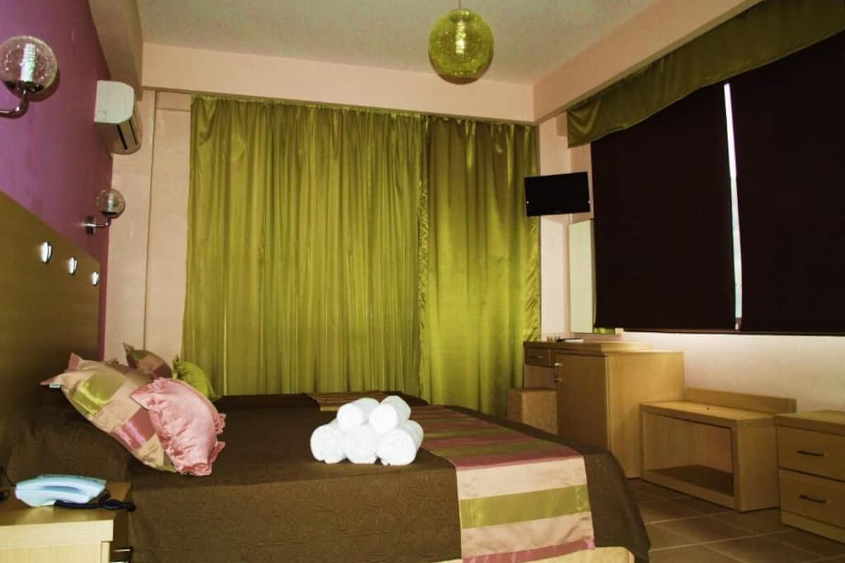 A bedroom with a bed, a desk, a chair, a TV, and a window with curtains.