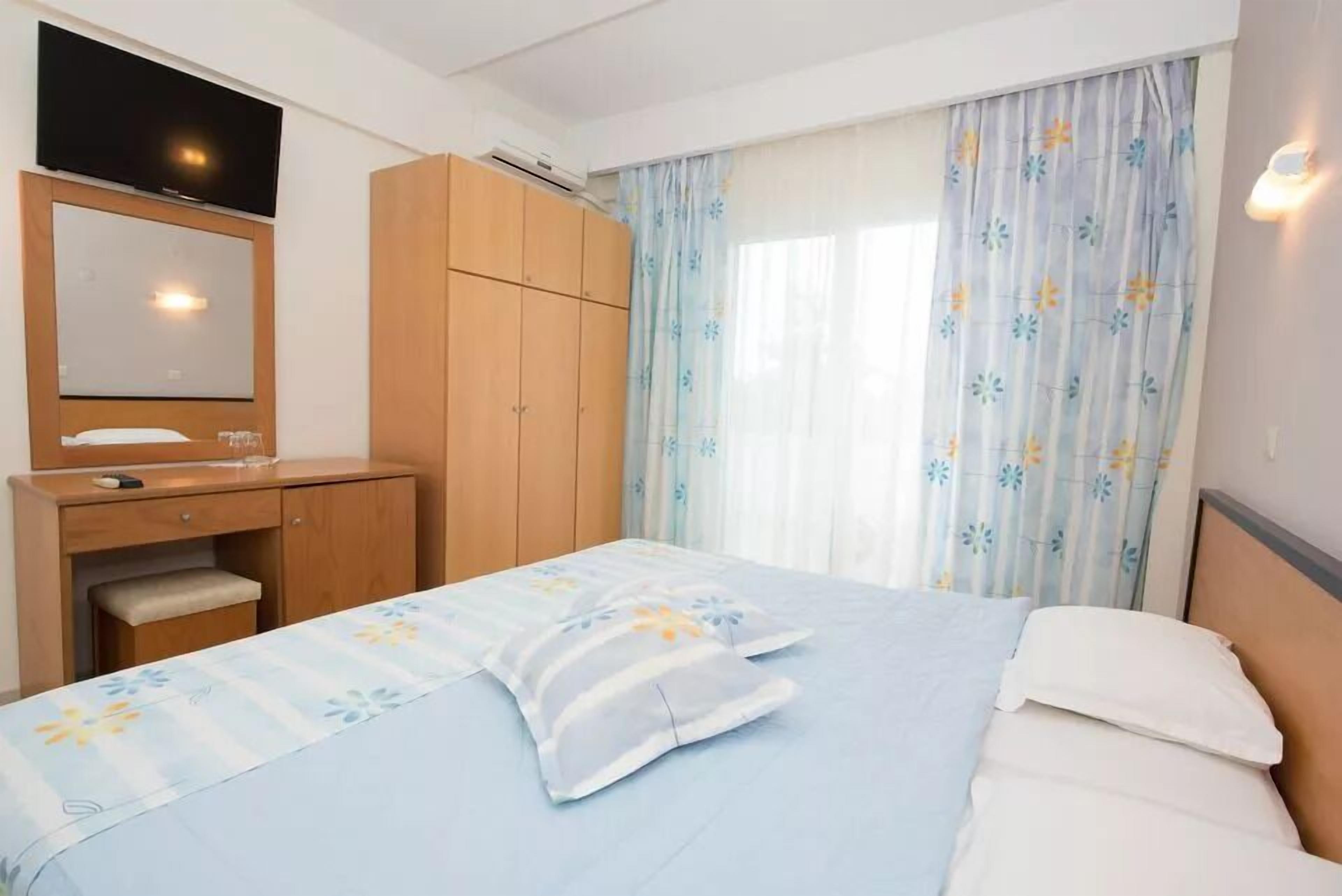 Une chambre d’hôtel avec un lit, une armoire en bois, un petit bureau avec un miroir et un téléviseur fixé au-dessus de l’armoire.