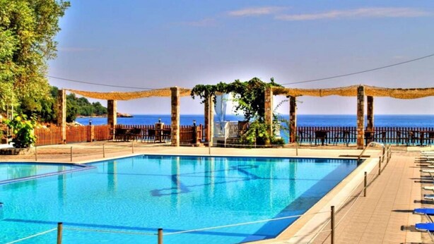A rectangular swimming pool with a clear blue water surface, surrounded by a wooden deck and a stone wall. - Maranton Beach Hotel (Thasos)