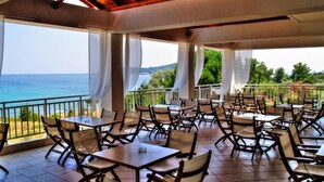 A covered outdoor dining area with tables and chairs, overlooking a scenic view of the sea. - Maranton Beach Hotel (Thasos)