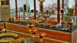 A buffet with various food items and drinks, a glass display case, and a view of an outdoor patio area. - Maranton Beach Hotel (Thasos)