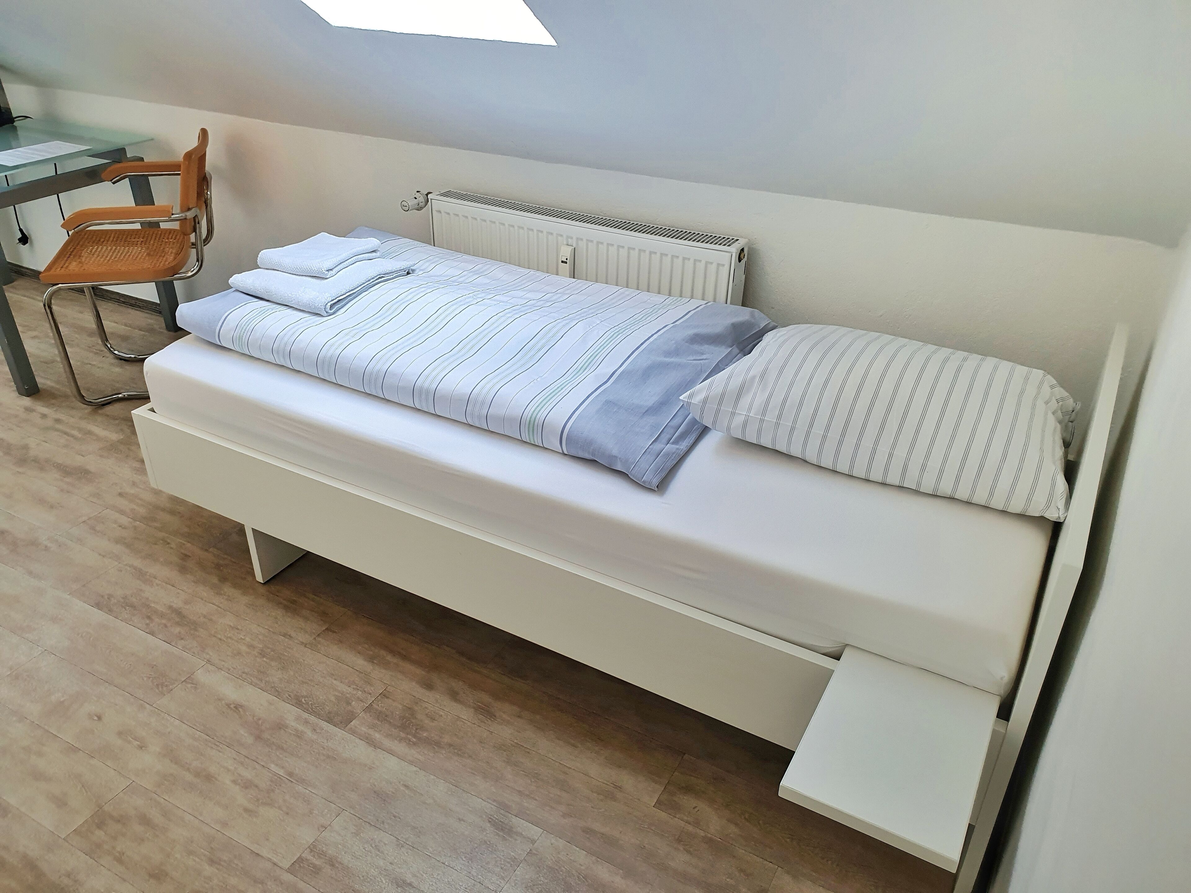 Ein kleines, ordentliches Schlafzimmer mit einem Einzelbett, einem Sessel und einer Heizung.