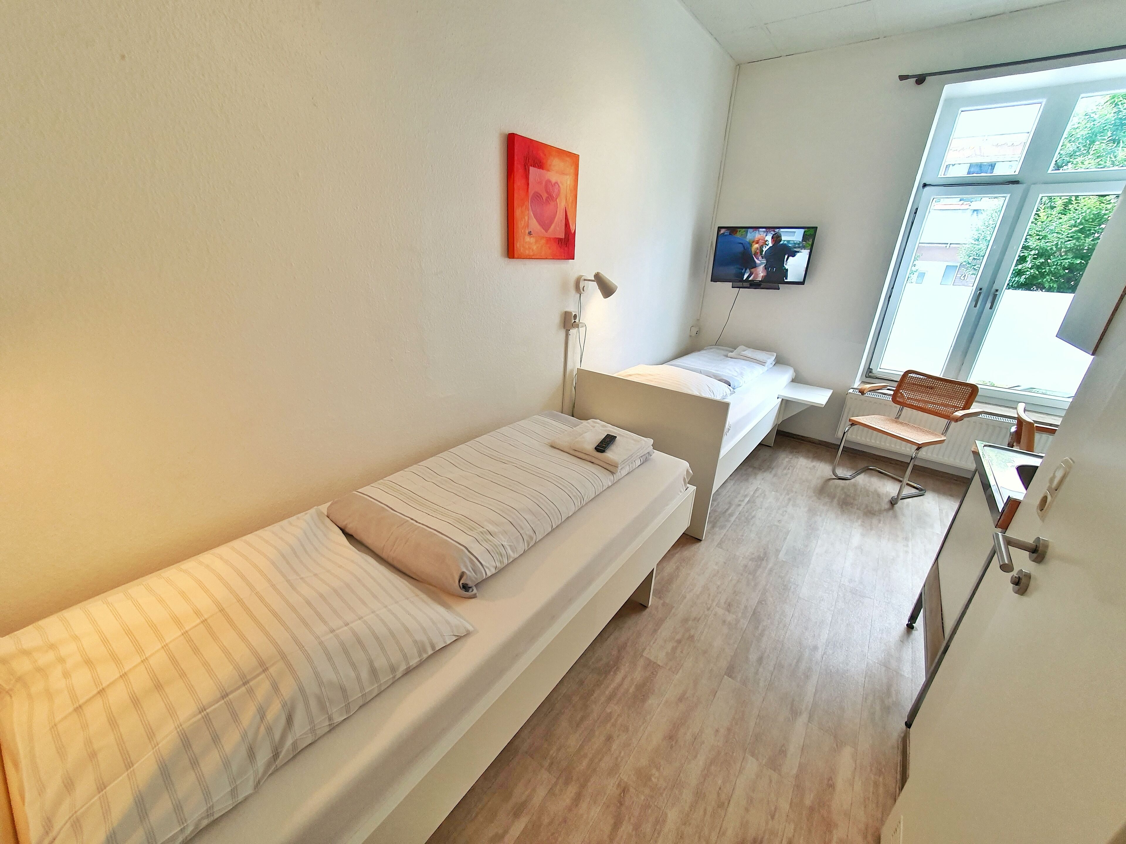 Ein Schlafzimmer mit einem Einzelbett, einem Schreibtisch, einem Stuhl, einem Fernseher und einem Fenster.